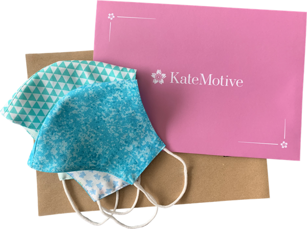 Two colorful face masks on top of a pink envelope, and a brown recycled paper envelope beneath
